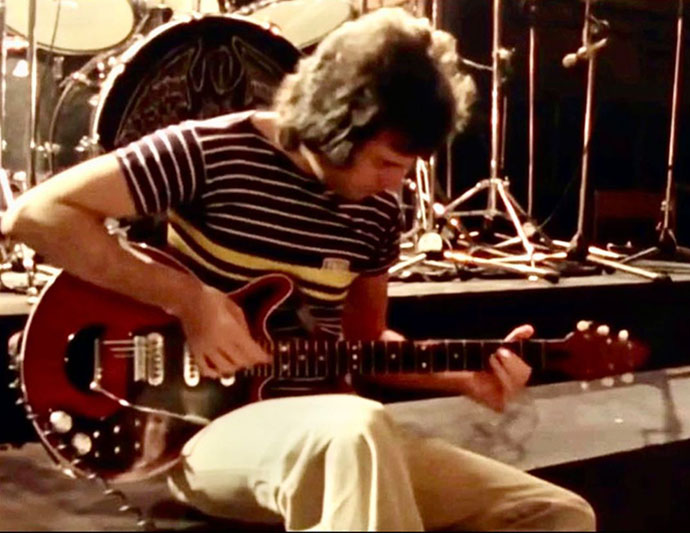 Freddie Mercury, seated with guitar